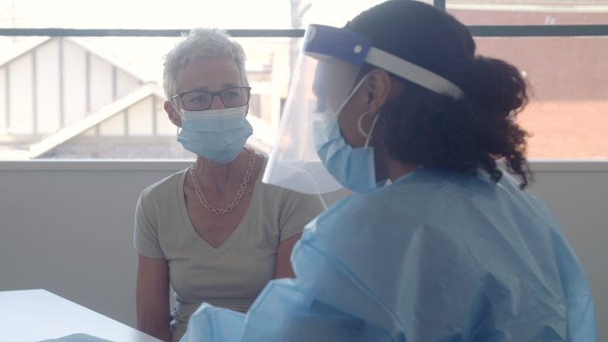 戴口罩的高级妇女与护士谈论新冠肺炎疫苗