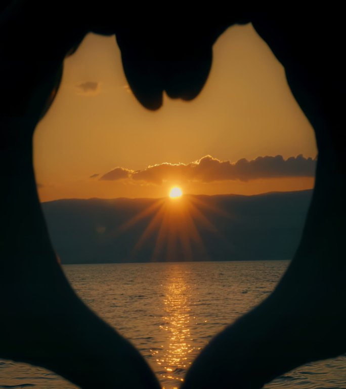 爱心之手表情符号。日落在水面上。竖的