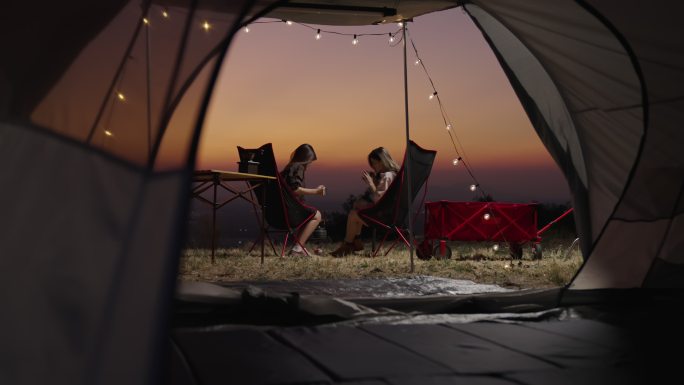 年轻的女人在旅游帐篷里休息，点燃篝火，在假日里和朋友们一起看日落。亚洲，露营，朋友，帐篷，日落，旅游