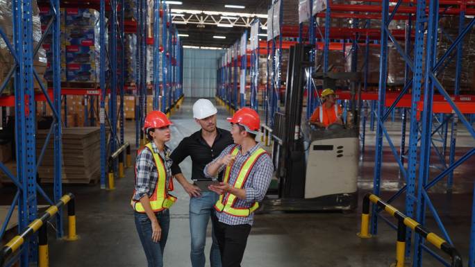 仓库经理与两名不同的员工用数字平板电脑交谈，讨论大型仓库仓库的交货时间表