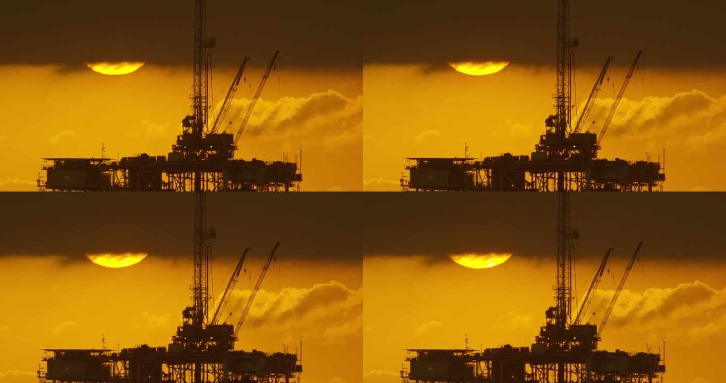 太阳从风暴云下露出，在戏剧性的暴风雨天空下日落时，前景中的海上石油钻井平台的剪影