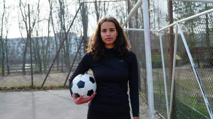 一位年轻女子足球运动员站在运动场球门柱旁的肖像