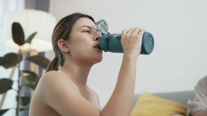 年轻的亚洲女人在休息时喝水，看着她的智能手表。