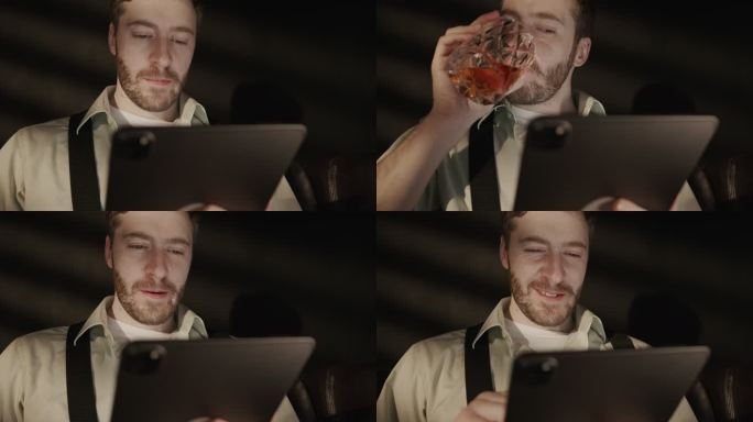 一个穿着衬衫和背带裤的饮酒男子躺在沙发上，在平板电脑上打字，喝了一杯威士忌