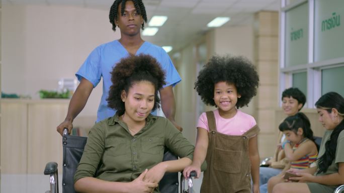 医疗技术人员沿着医院走廊移动患者的轮椅，而患者的妹妹则在旁边微笑。