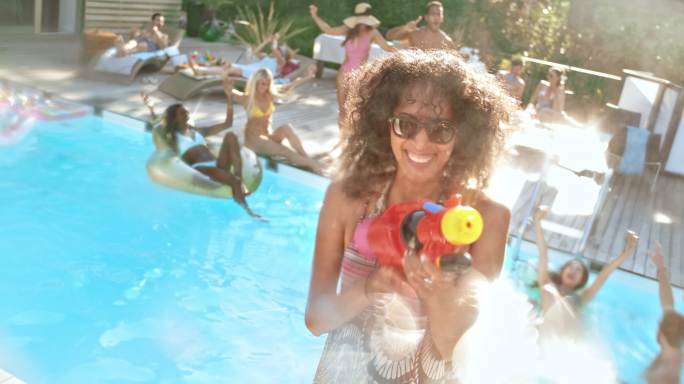 SLO MO一位戴着墨镜的女子在泳池派对上用水枪向镜头喷水