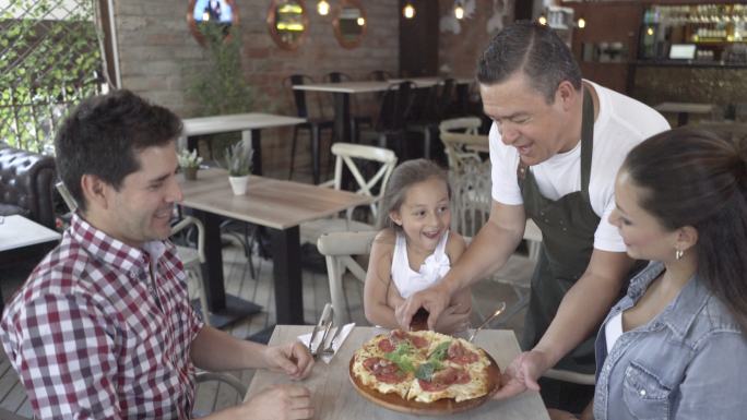 服务员在餐厅给一个漂亮的家庭送披萨