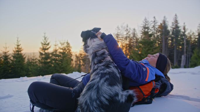 日出时分，一位年轻女子和她的狗在雪坡上拥抱