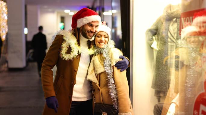 一对戴着圣诞帽的年轻夫妇正在城市街道上享受购物