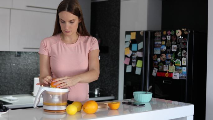 一位孕妇在厨房里切柠檬和橙子，做一种健康清爽的饮料