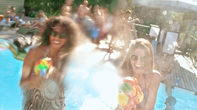 两名女子在泳池派对上玩得很开心，并用水枪向镜头泼水