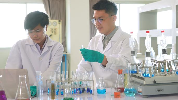 一名亚洲医学科学家小组的研究人员身穿实验服和防护设备，仔细检查、测量液体和笔记本电脑，寻找潜在的新冠