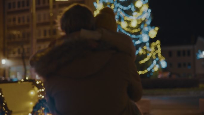 SLO MO夫妇在城市广场拥抱亲吻，背景是圣诞树和灯光