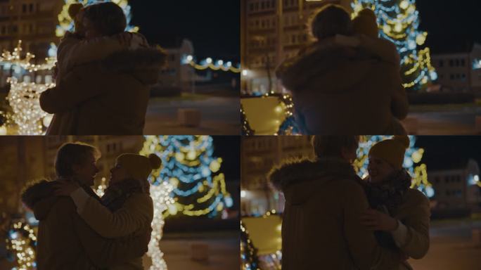 SLO MO夫妇在城市广场拥抱亲吻，背景是圣诞树和灯光