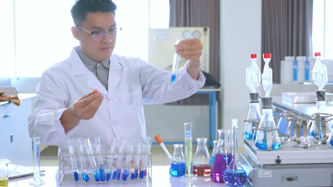 一名亚洲男性医学科学家，穿着实验室工作服和防护设备，仔细检查、测量并使用液体，寻找潜在的新冠肺炎疫苗