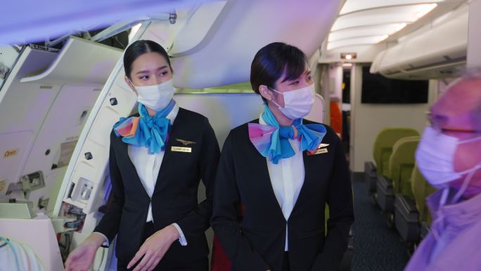 两名亚洲空姐带着防护面罩微笑着，热烈欢迎乘客下飞机抵达机场，踏上新冠肺炎大流行时代的新征程。
