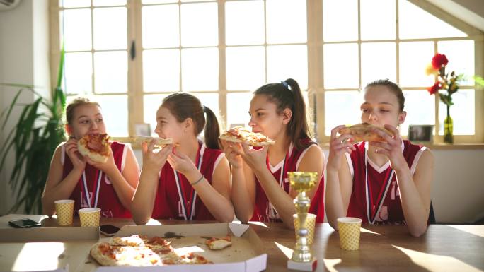 可爱的女孩篮球运动员在赢得奖杯后和教练一起吃披萨