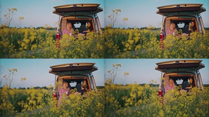 远景：两位女士欣赏停在油菜花田里的露营车的景色
