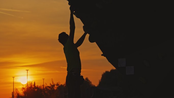 SLO MO登山者准备在日落时在室外攀岩墙上攀爬
