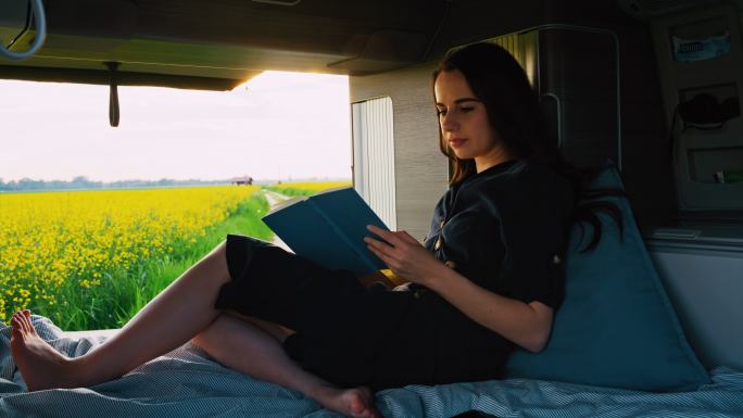DS女子在停在油菜花田边的露营车的小屋里看书
