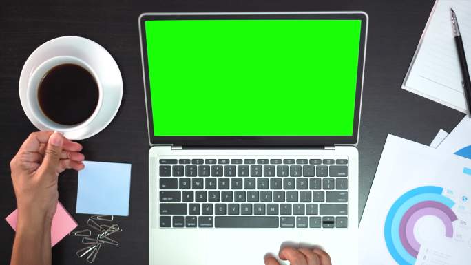 从上方看，在白色办公桌上使用绿色屏幕的笔记本电脑的男性双手