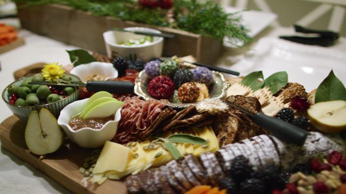 在室内圣诞庆典/派对上，摄像机围绕着桌上的各种水果、酱汁和装饰的开胃菜烤肉/奶酪板