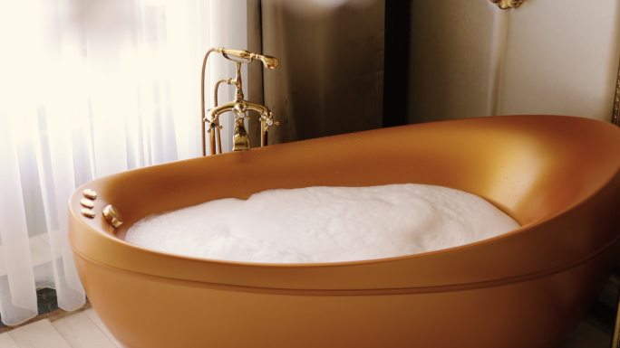 浴缸里有白色软泡沫。金色浴缸，豪华酒店客房，酒店套房