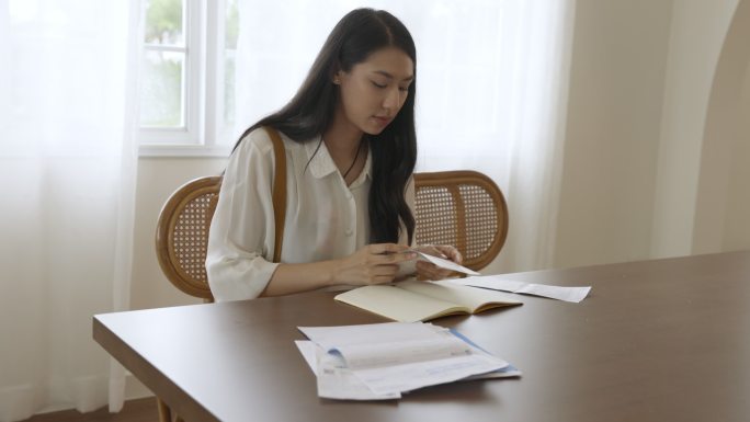 该女子从服务提供商发送的账单中记录了费用，并在笔记本上进行了记录