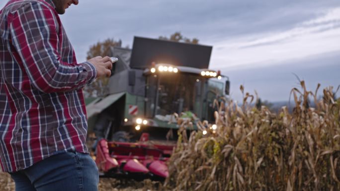 农民在联合收割机上使用手机收割玉米作物