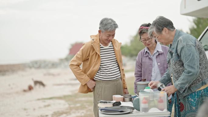 周末，亚洲的中国老年朋友在海滩的房车前准备咖啡