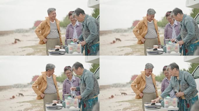 周末，亚洲的中国老年朋友在海滩的房车前准备咖啡