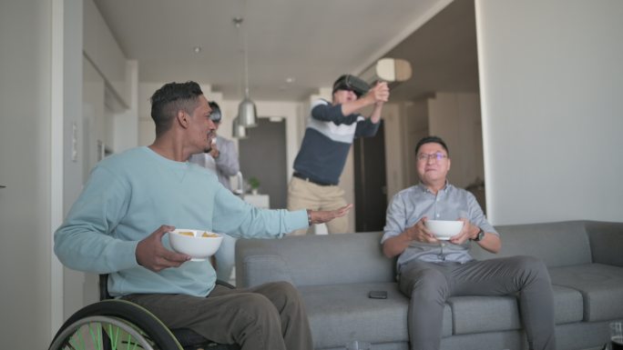 一群亚洲朋友坐在沙发上的客厅里一起玩VR视频游戏
