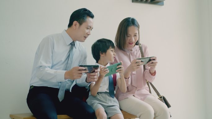微笑而幸福的亚洲家庭，年轻的父亲，美丽的母亲，可爱的小儿子，在家里一起用智能手机作为游戏控制器，在长