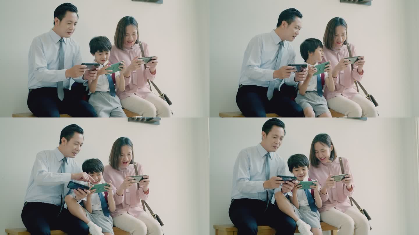 微笑而幸福的亚洲家庭，年轻的父亲，美丽的母亲，可爱的小儿子，在家里一起用智能手机作为游戏控制器，在长