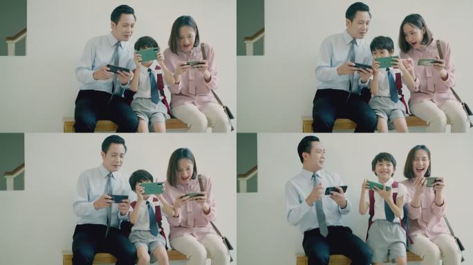 一个年轻的亚洲家庭和一个可爱的小男孩在家里一起坐在长椅上，用智能手机玩电子游戏。快乐的爸爸、妈妈和他