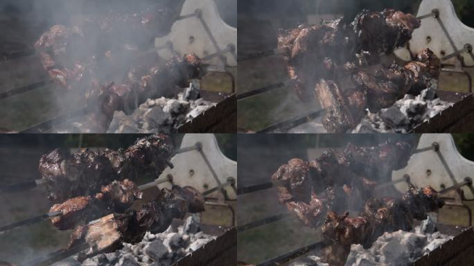 三个缓慢旋转的烤串的斜视图，羊肉被烟雾笼罩，在露天木炭上烹饪时滴落
