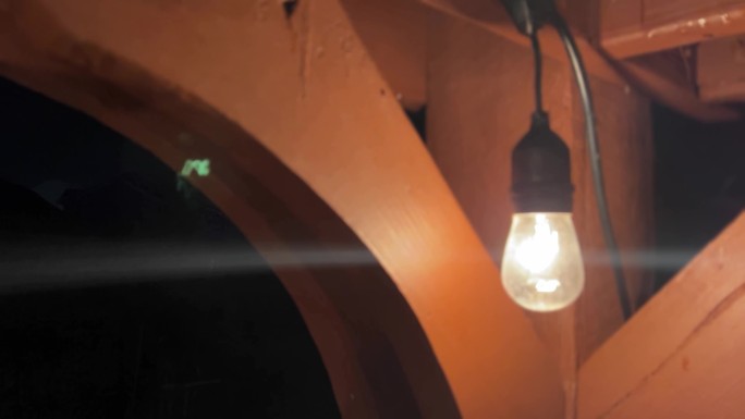黑暗中，爱迪生灯泡在后院木制凉棚上悬挂的照明电缆上闪耀