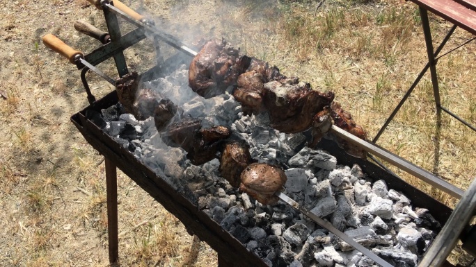 潘宁在三个缓慢旋转的烤串上射击，羊肉在木炭上烘烤时冒着烟，滴水