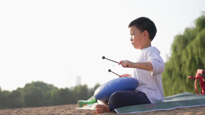 男孩在夕阳西下的海边沙滩上演奏空灵鼓