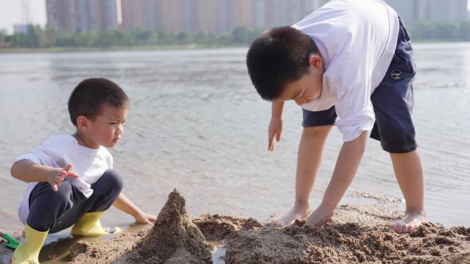 小男孩在河边的沙滩上挖沙子堆城堡