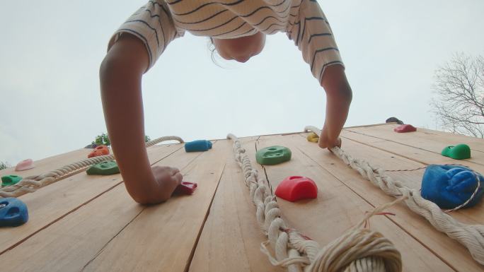 亚洲小女孩爬上游乐场所小木墙的视角照片。