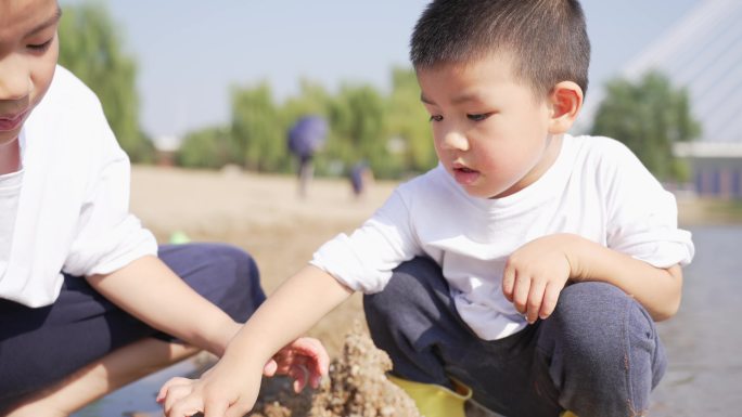 小男孩在河边的沙滩上挖沙子堆城堡