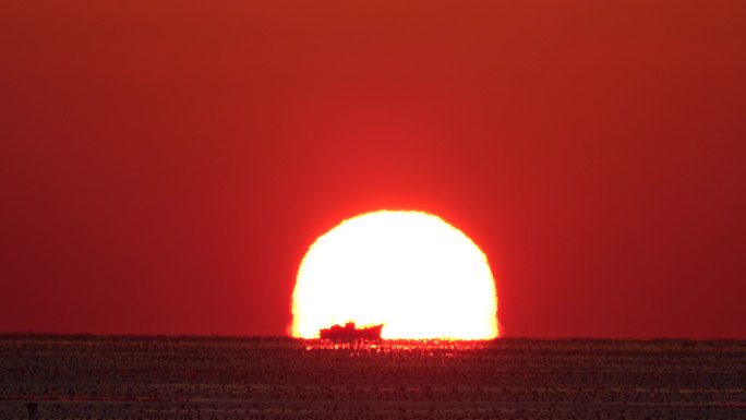一艘小船穿过海边初升的太阳