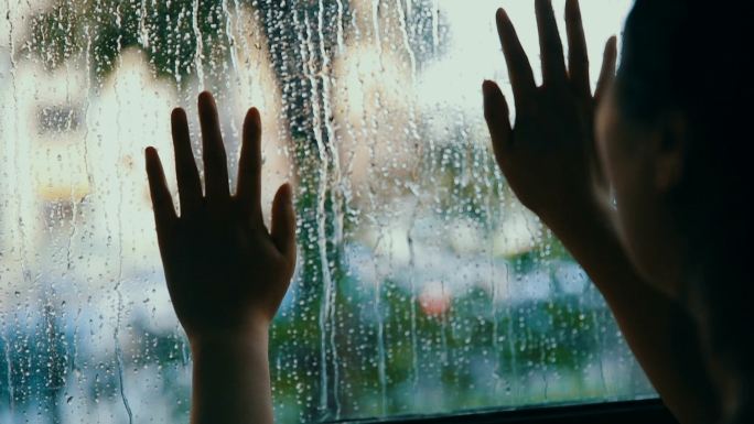 女人用雨滴触摸窗户