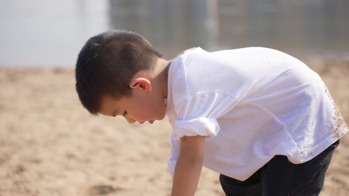 小男孩在河边的沙滩上挖沙子堆城堡