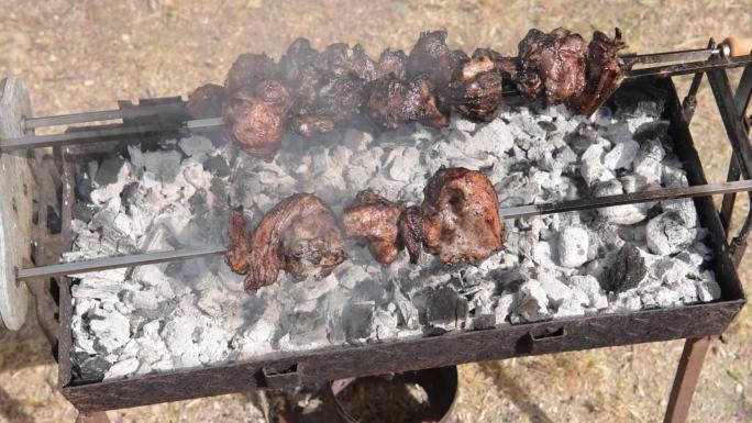 从上方观看三个缓慢旋转的烤串，羊肉在木炭上烤时冒烟并滴落