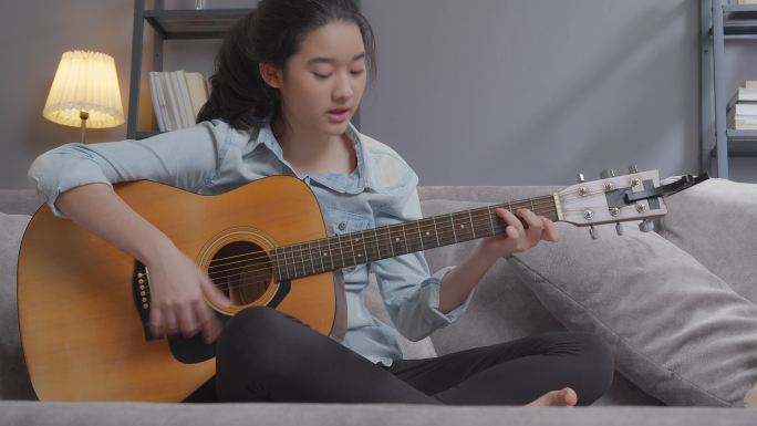 快乐的青少年女孩在家里的客厅里弹吉他，有创造性的爱好