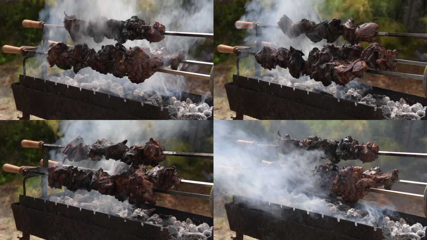 三个缓慢旋转的烤串的斜视图，羊肉在露天木炭上烤时冒烟并滴落