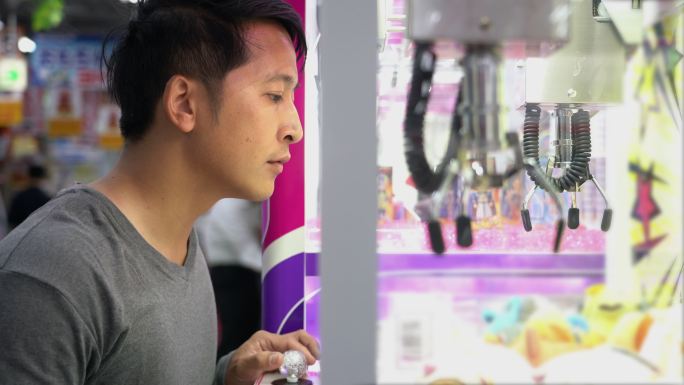 一名亚洲游客在日本街机上玩鹤爪游戏机