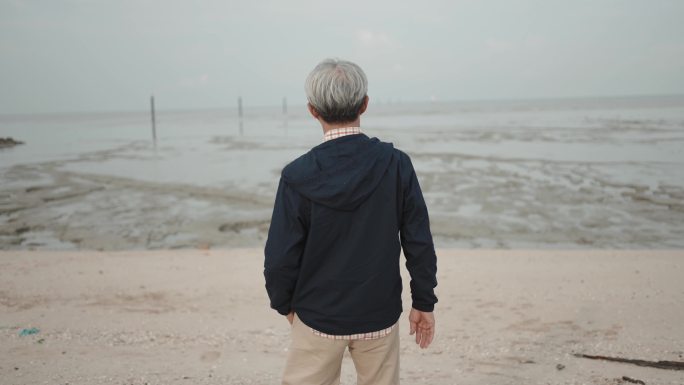 站在沙滩上看海的亚洲中国老人的后视图